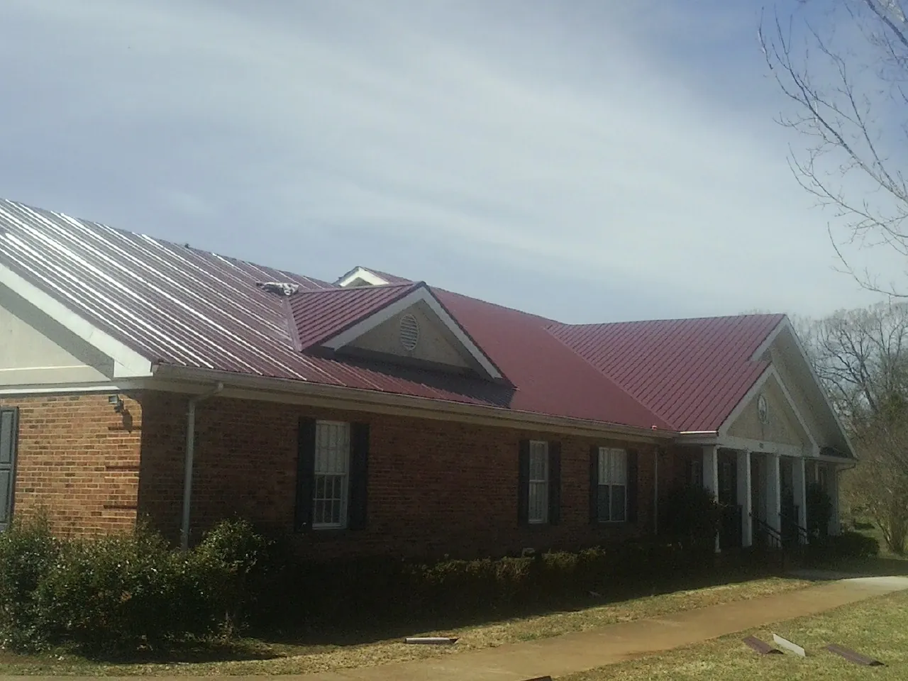 Red metal roof with gabled entries on a long brick building, from a Hail Damage Roof Repair job in Darien