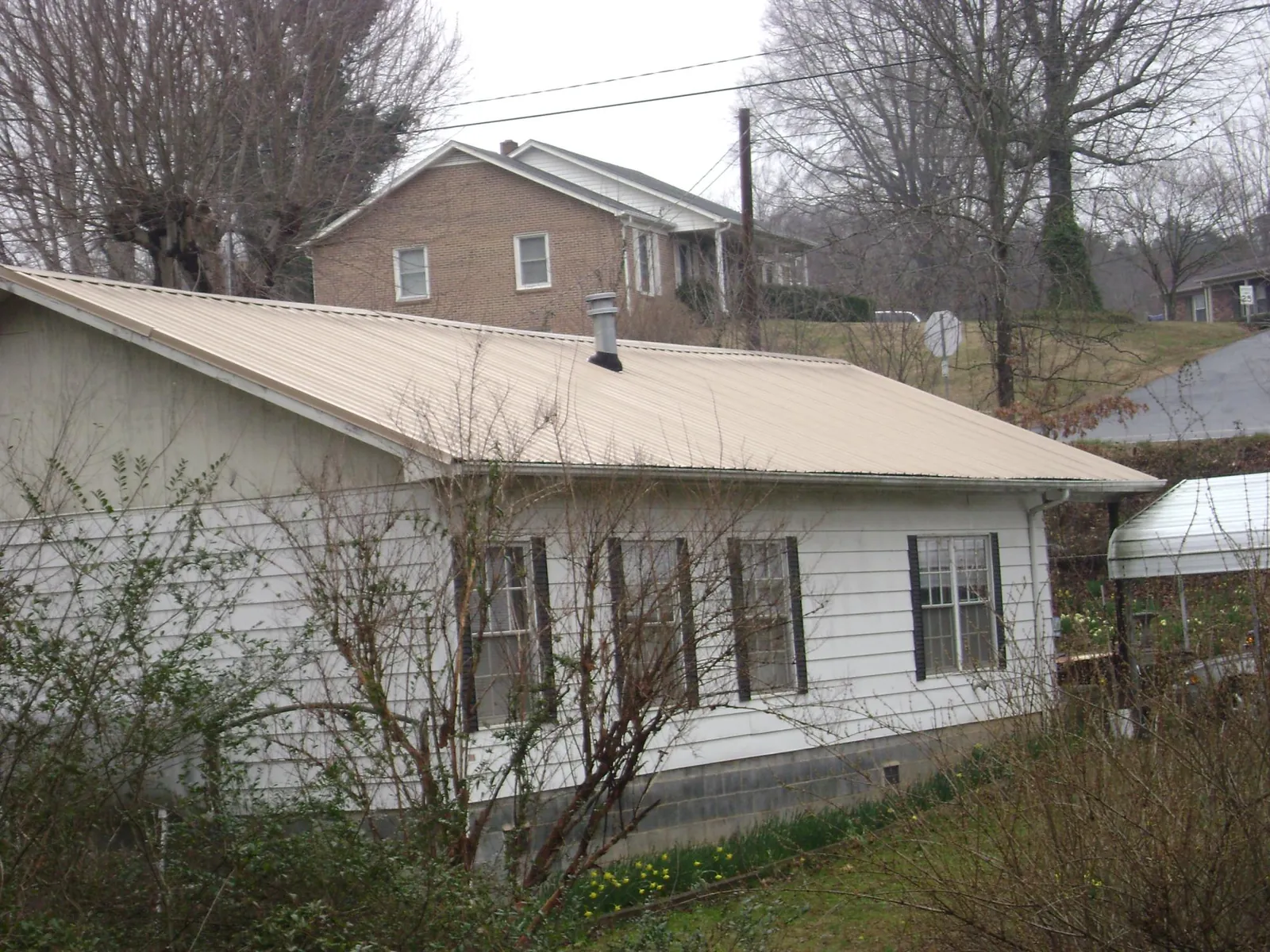 Tan metal roof on a white sided house set into a hillside — Commercial Roofing by Roofing Brothers in Darien